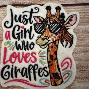 May include: Embroidered patch with a pink, white and black design. The text reads "Just a Girl Who Loves Giraffes". A cartoon giraffe wearing sunglasses is featured on the right side of the patch.
