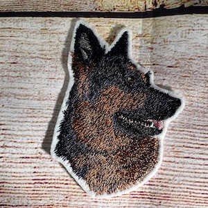 May include: Embroidered patch of a German Shepherd dog's head, with brown and black fur, looking to the right. The patch is on a white background.