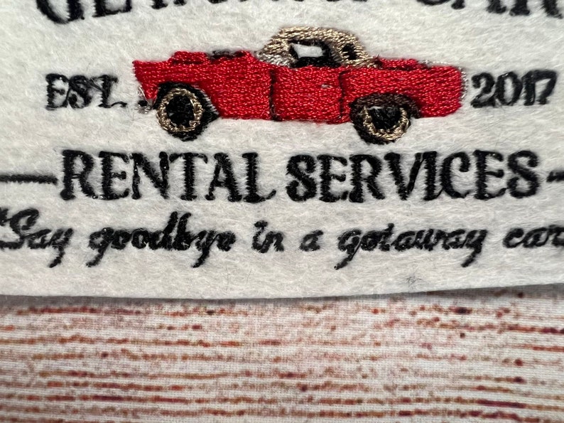 May include: Embroidered logo for a car rental company called "Get Away Cars" established in 2007. The logo features a red vintage car with the text "Rental Services" and the tagline "Say goodbye in a getaway car."