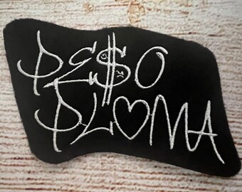 Puede incluir: Parche de tela negro con texto bordado en blanco que dice "Peso Plomo" con un signo de dólar estilizado y un corazón.