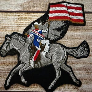 Può includere: Toppa ricamata raffigurante un cavaliere su un cavallo grigio, che tiene una bandiera a strisce rosse e bianche. Il cavaliere indossa un cappello bianco, un completo blu e bianco e stivali rossi. La toppa ha un bordo nero.