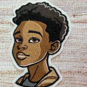 May include: Embroidered patch of a young person with brown skin, black hair, and a light brown jacket. The patch is on a white background.