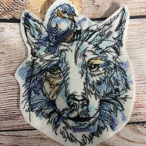 May include: Embroidered patch featuring a wolf's head with a bluebird perched on top. The wolf's fur is depicted in shades of blue and grey, with a hint of gold in the eyes. The bluebird is a vibrant blue with a white belly.