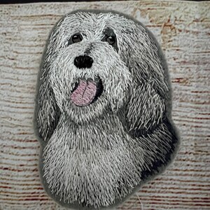 Peut inclure: Patch brodé représentant la tête d'un chien avec une fourrure blanche et grise, un nez noir et une langue rose. Le chien regarde directement le spectateur.
