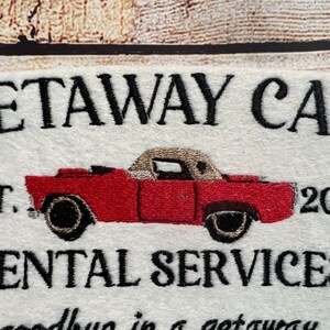 Puede incluir: Un letrero blanco con texto bordado en negro que dice "Getaway Car Est. 2017 - Rental Services -" con una ilustraci&oacute;n de un coche rojo convertible.