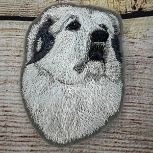 Puede incluir: Parche bordado de la cabeza de un perro de montaña de los Pirineos, con pelaje blanco y marcas negras. El perro está mirando hacia arriba con la boca cerrada.