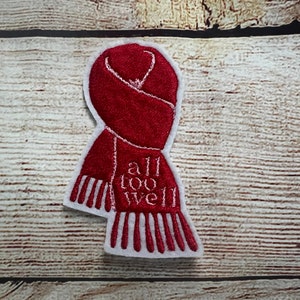 Puede incluir: Parche bordado rojo con un contorno blanco de una bufanda y el texto "all too well" en blanco.