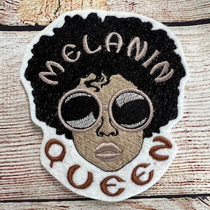 Könnte beinhalten: Gestickter Aufnäher mit einer Cartoon-Illustration einer Person mit Afro-Frisur, die eine Sonnenbrille trägt. Der Text "MELANIN QUEEN" ist in braunem Garn um das Bild gestickt.