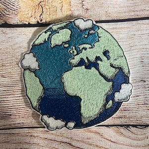 Könnte beinhalten: Gestickter Aufnäher einer blauen und grünen Erde mit weißen Wolken. Die Kontinente sind grün umrandet und die Ozeane sind blau.