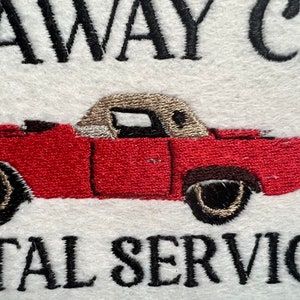 Puede incluir: Dise&ntilde;o bordado de un coche rojo convertible con capo beige. El texto "getaway car rental service" est&aacute; bordado debajo del coche.