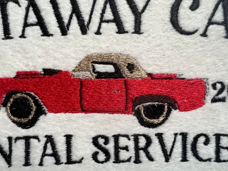 Puede incluir: Dise&ntilde;o bordado de un coche rojo convertible con capo beige. El texto "getaway car rental service" est&aacute; bordado debajo del coche.
