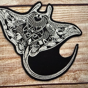 Peut inclure: Écusson brodé noir et blanc représentant une raie manta. Le patch présente des détails complexes avec un motif brodé blanc sur un fond noir. Idéal pour les vêtements ou les accessoires.
