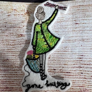 Könnte beinhalten: Gestickter Aufnäher einer Person, die Stricknadeln und Wolle hält, mit dem Text "gone knitting".