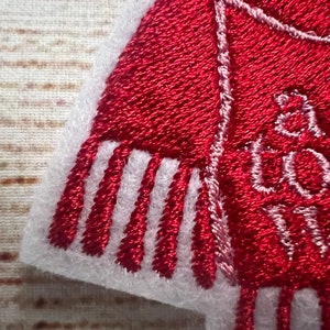 Puede incluir: Parche de fieltro rojo bordado con puntadas blancas. El parche presenta una bufanda roja con flecos blancos y el texto "All I want for Christmas is you".