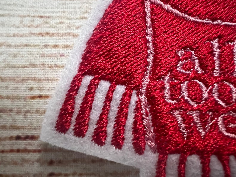 Puede incluir: Parche de fieltro rojo bordado con puntadas blancas. El parche presenta una bufanda roja con flecos blancos y el texto "All I want for Christmas is you".