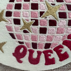 Pu&ograve; includere: Toppa ricamata da stirare con un design a palla da discoteca rosa e bordeaux con stelle dorate e la parola "QUEEN" in rosa.