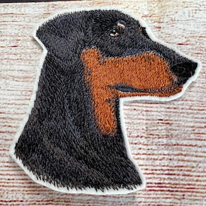 May include: Embroidered patch of a black and brown Doberman Pinscher dog's head, viewed in profile.