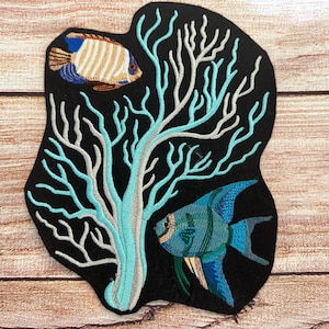May include: Embroidered patch featuring a blue and green angelfish and a white and brown butterfly fish swimming near a turquoise coral branch on a black background.
