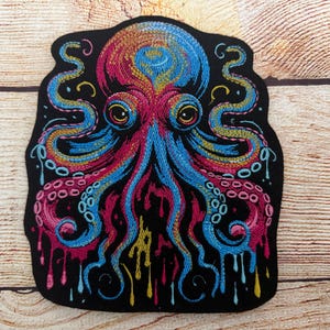 May include: Embroidered octopus patch with a black background. The octopus is depicted in vibrant colors, including blue, pink, yellow, and orange. The tentacles have suction cups and the design has a dripping effect. The patch is on a wooden surface.