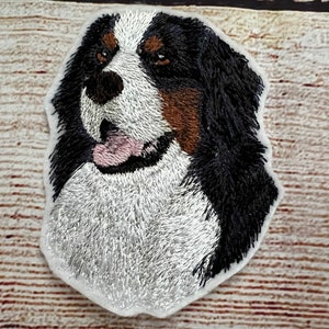 Könnte beinhalten: Gestickter Aufnäher mit dem Gesicht eines Berner Sennenhundes. Der Hund hat schwarzes, weißes und braunes Fell mit einer rosa Zunge. Der Aufnäher befindet sich auf weißem Hintergrund.