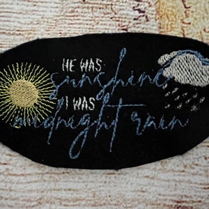 May include: Black fabric patch with embroidered yellow sun, blue rain cloud, and the text "He was sunshine, I was midnight rain."