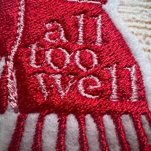 Puede incluir: Bufanda roja bordada con flecos blancos y el texto "all too well" en hilo blanco.