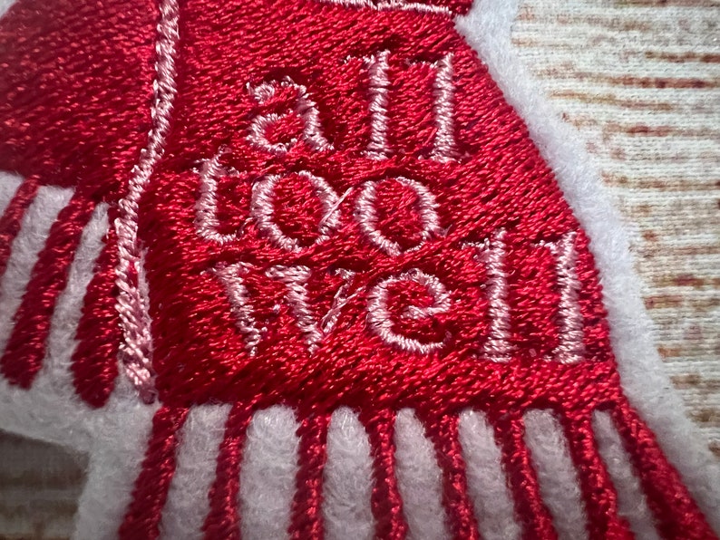 Puede incluir: Bufanda roja bordada con flecos blancos y el texto "all too well" en hilo blanco.