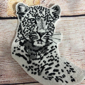 May include: A white embroidered patch of a black and white leopard with a close-up of its face.