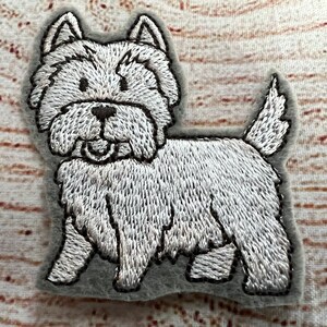May include: Embroidered patch of a West Highland White Terrier dog. The patch is white with black detailing and a gray border. The dog is depicted in a standing pose with its tongue slightly visible.