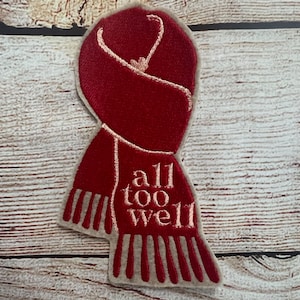 May include: Red and white embroidered patch of a scarf with the text "all too well" on it.