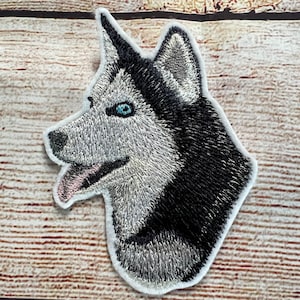 Puede incluir: Parche bordado de la cabeza de un perro husky, con ojos azules, lengua rosa y pelaje blanco y negro.
