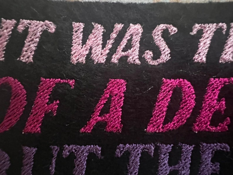 Puede incluir: Parche bordado con hilo rosa y morado. El texto dice "It was the best of a dea..."