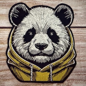 May include: Embroidered patch of a panda bear wearing a yellow hoodie. The panda has black eyes and a black nose.