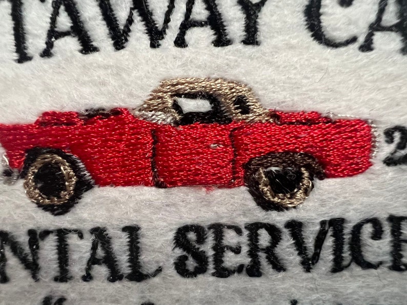 May include: Embroidered logo for a car rental service. The logo features a red convertible car with a tan top and the text "Stay Away Car Rental Service".