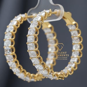 Peut inclure: Boucles d'oreilles créoles dorées incrustées de pierres précieuses claires de taille carrée. Les boucles d'oreilles sont présentées sur un fond sombre. Le texte "OPULENT ORNAMENTS" et "FINE DIAMOND JEWELRY HANDCRAFTED FOR USA" est visible.