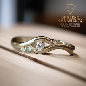Op de afbeelding: Een goudkleurige ring met een uniek ontwerp, met een centrale diamant en kleinere accentstenen. De ring heeft een vloeiende, organische vorm. De tekst "OPULENT ORNAMENTS" en "FIND DIAMOND JEWELRY HANDCRAFTED FOR USA" is zichtbaar.