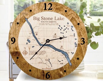 May include: A wooden clock with a map of Big Stone Lake, South Dakota. The clock face is brown with black numbers and hands. The map is beige with blue water features. The text "Big Stone Lake, South Dakota" is printed on the clock face.