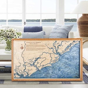 May include: A framed wooden map of Charleston Harbor, South Carolina, with blue and brown details. The map is surrounded by a light brown wooden frame.