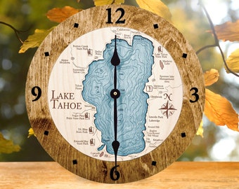 May include: A round wooden clock featuring a detailed map of Lake Tahoe. The clock face displays the lake's contours in blue, with place names and depth markings. The clock has black hands and a wooden frame, with the numbers 3, 6, 9, and 12 marked.