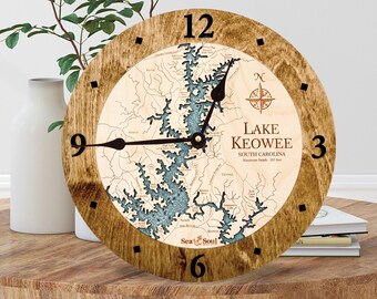 May include: A wooden clock with a map of Lake Keowee, South Carolina. The clock face is brown with black numbers and hands. The map is blue and white with the lake's name and maximum depth printed on it. The clock is surrounded by a brown wooden frame.
