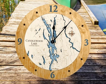 May include: A wooden clock with a map of Candlewood Lake, Connecticut. The clock face is surrounded by a light brown wooden frame with black hour markers. The clock hands are black and the clock face is white with blue water features.