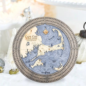 May include: A wooden cribbage board with a map of Cape Cod and the Islands, Massachusetts. The board has a compass rose, a compass, and the words "Sea & Soul" on it.