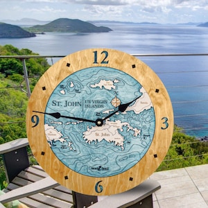 May include: A wooden clock with a map of the US Virgin Islands on the face. The clock is surrounded by a light brown wooden frame and has black hands. The clock face is blue and white and shows the islands of St. John, St. Thomas, and Tortola. The clock is labeled "St. John US Virgin Islands" and "Sea & Soul".