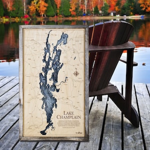 May include: A wooden map of Lake Champlain in a rustic frame. The map is laser-cut and shows the lake's outline and surrounding areas. The map is on a wooden dock with a wooden chair in the background.