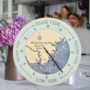 May include: A light blue wooden tide clock with a map of Kennebunk Beach, Maine. The clock face has numbers 0-5 and arrows indicating high tide, low tide, rising tide, and falling tide.