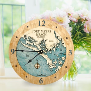 May include: A wooden clock with a nautical map design featuring the coastline of Fort Myers Beach, Florida. The clock face is blue and white with a compass rose and the words "Sea & Soul".