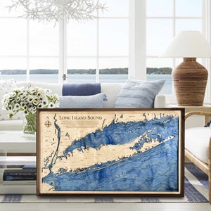 May include: A wooden map of Long Island Sound with blue water and brown land features. The map is framed in a dark brown frame and is hanging on a wall.