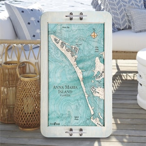 May include: A rectangular wooden wall art piece featuring a detailed map of Anna Maria Island, Florida, in shades of blue and white. The map is framed in a light-colored wood with metal hardware. The text "Anna Maria Island FLORIDA" is visible.