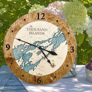 Puede incluir: Un reloj de madera con un mapa de las Mil Islas en la esfera. El reloj tiene agujas negras y un dise&ntilde;o de br&uacute;jula en el centro. El reloj est&aacute; rodeado por un marco de madera marr&oacute;n.