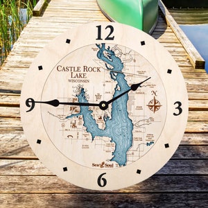 May include: A round wooden clock with a map of Castle Rock Lake, Wisconsin, in blue and tan tones. The clock face features black hands, black numerals, and a compass rose. The clock is on a wooden dock.